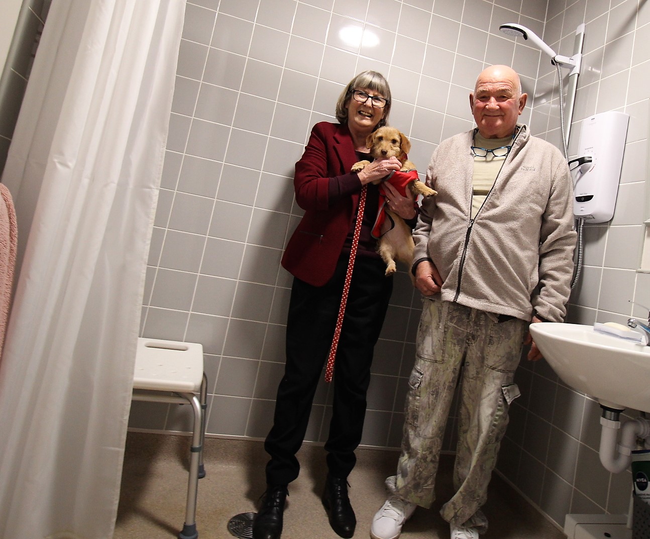•	Left to right – Portfolio Holder for Sustainable Growth and Economy, Councillor Jenny Hollingsworth with resident Robert Watling (and Sandy the dog) in a newly converted wet room,